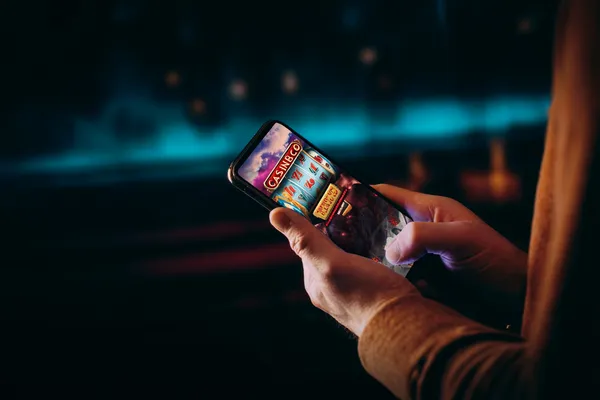 ক্যাসিনো-থিমযুক্ত ব্যাকগ্রাউন্ডে কেউ তার ডিভাইস ব্যবহার করছেন—যা CT44–এ মসৃণভাবে অ্যাকাউন্টে পুনরায় প্রবেশের অভিজ্ঞতাকে তুলে ধরে।